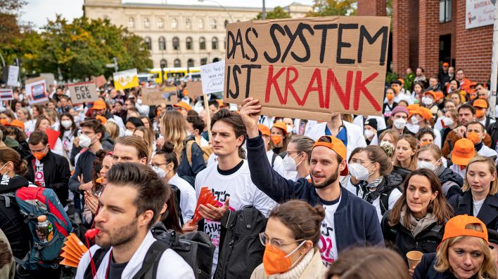 Ärzte stehen am 05.10.2022 bei einem eintägigen Warnstreik des Marburger Bunds an der Charité mit einem Schild mit der Aufschrift "Das System ist krank". (Quelle: dpa/Fabian Sommer)