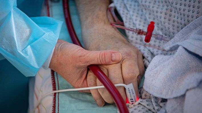 Symbolbild:Eine Krankenschwester versorgt einen schwer erkrankten Patienten auf der Intensivstation und hält dabei die Hand des Mannes.(Quelle:dpa/B.Roessler)