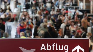 Am Flughafen Berlin Brandenburg BER stehen zahlreiche Reisende in einer Schlange zur Sicherheitskontolle hinter einem Schild mit der Aufschrift "Abflug". (Quelle: dpa/Jörg Carstensen)