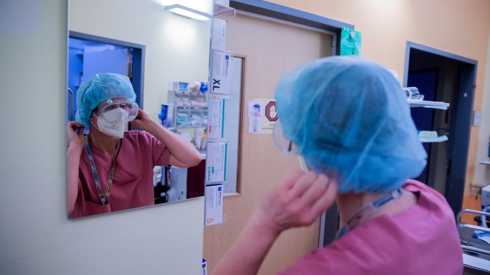 Symbolbild: Eine Intensivfachpflegerin legt auf der Intensivstation Schutzkleidung an bevor sie das Zimmer eines Covid-19-Patienten betritt. (Quelle: dpa/C. Soeder)