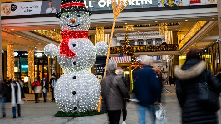 Archivbild: Vor dem Einkaufszentrum «Mall of Berlin» steht ein leuchtender Schneemann, daneben gehen Leute, die noch kurz vor Weihnachten zum Einkaufen unterwegs sind. (Quelle: dpa/C. Gateau)