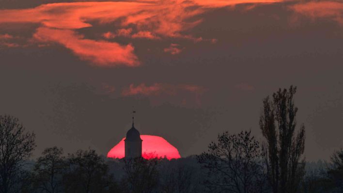 Hohenjesar: Farbenprächtig leuchtet die untergehende Sonne hinter der Spitze der barocken Dorfkirche. (Foto: Patrick Pleul/dpa)