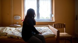 Archivbild: Eine Frau sitzt am 12.11.2015 in einem Frauenhaus auf einem Bett. Frauenhäuser bieten Schutz, wenn der Partner zur Gefahr wird. (Quelle: dpa/Maja Hitij)