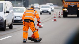 Symbolbild: Ein Arbeiter sammelt am 01.11.2022 bei der Enthüllung des letzten und vierten Autobahnbärs Berlins an der grunderneuerten A114 Leitkegel. (Quelle: dpa/Christoph Soeder)