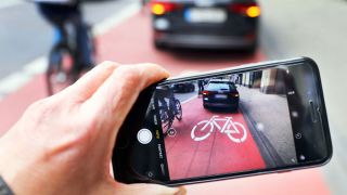 Symbolbild:Auf einem Smartphone ist das Bild eines Autos zu sehen, das auf einem Radstreifen hält.(Quelle:dpa/O.Berg)
