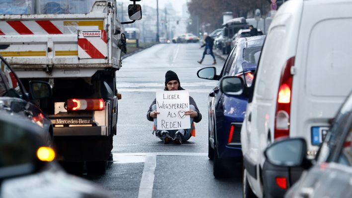 Ein Aktivist zeigt ein Schild mit der Aufschrift „Lieber Wegsperren als Reden“ bei einer Sitzblockade mit weiteren Aktivisten.(Quelle:dpa/C.Koall)
