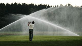 Archivbild: Freizeitsportler spielt auf einer Golfanlage, während die Rasensprenger den Platz bewässern. (Quelle: imago images/Action pictures)