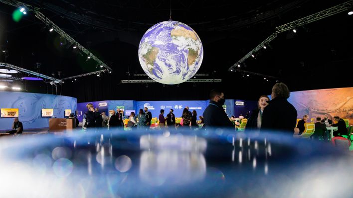Archivbild: Menschen stehen bei der UN-Klimakonferenz COP26 unter einem Globus. (Quelle: dpa/C. Soeder)