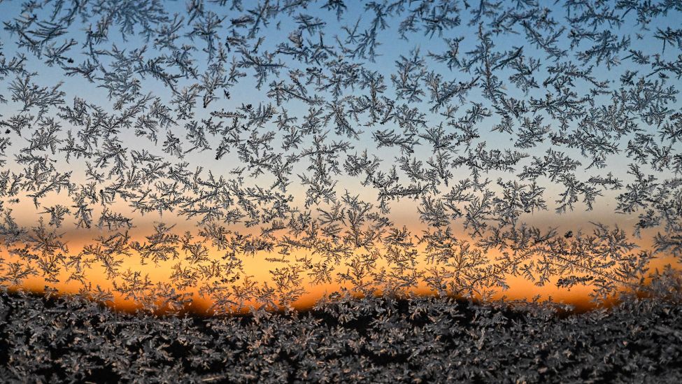 Eisblumen sind an einer Autoscheibe vor dem Sonnenaufgang zu sehen. (Quelle: dpa/P. Pleul)