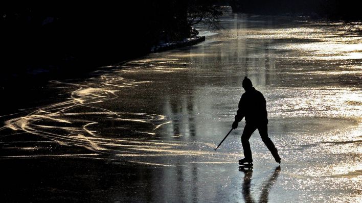 Einsamer Eishockeyspieler auf einem zugefrorenem See im abendlichen Brandenburg (Quelle: imago images/imagebroker)