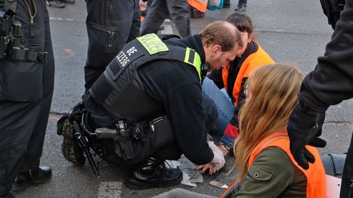Ein Polizist löst am 03.11.2022 die festgeklebte Hand einer Klimaaktivistin vor dem Berliner Hauptbahnhof vom Asphalt. (Quelle: rbb24/Caroline Winkler)
