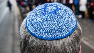 Symbolbild: Ein Mann mit Kippa steht am 20.10.2019 vor der Neuen Synagoge vor einer Menschenkette. (Quelle: dpa/Paul Zinken)