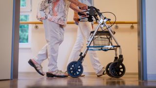 Eine Pflegekraft geht in einem Pflegeheim mit einer älteren Dame über einen Korridor. (Quelle: dpa/Christoph Schmidt)