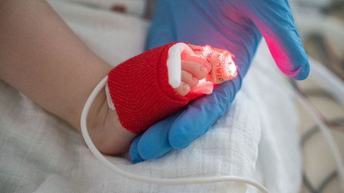 Eine Intensivpflegerin hält am 25.11.2021 auf der Kinder-Intensivstation des Olgahospitals des Klinkums Stuttgart den Fuß eines am Respiratorischen Synzytial-Virus (RS-Virus oder RSV) erkrankten Patienten, der beatmet wird, in der Hand. (Quelle: dpa/Marijan Murat)