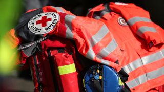 Symbolbild: Schriftzug Deutsches Rotes Kreuz an einer Jacke und Rea-Koffer einer Rettungskraft (Quelle: dpa/Andreas Gora)