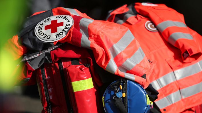 Symbolbild: Schriftzug Deutsches Rotes Kreuz an einer Jacke und Rea-Koffer einer Rettungskraft (Quelle: dpa/Andreas Gora)