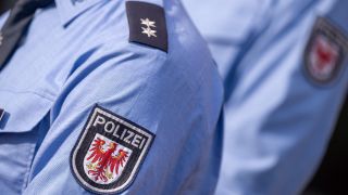 Das Logo der Brandenburger Polizei mit rotem Adler und Schriftzug auf der Uniform eines Polizeibeamten. (Quelle:dpa/Monika Skolimowska)