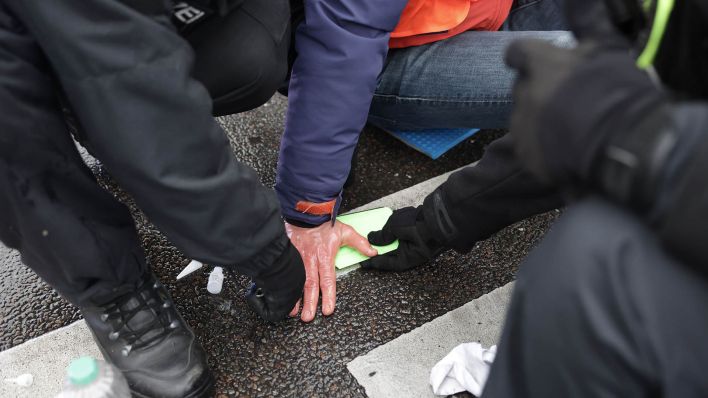 Archivbild: Polizisten lösen die Hand eines Klimaaktivisten vom Asphalt auf der Invalidenstraße. (Quelle: dpa/Jörg Carstensen)