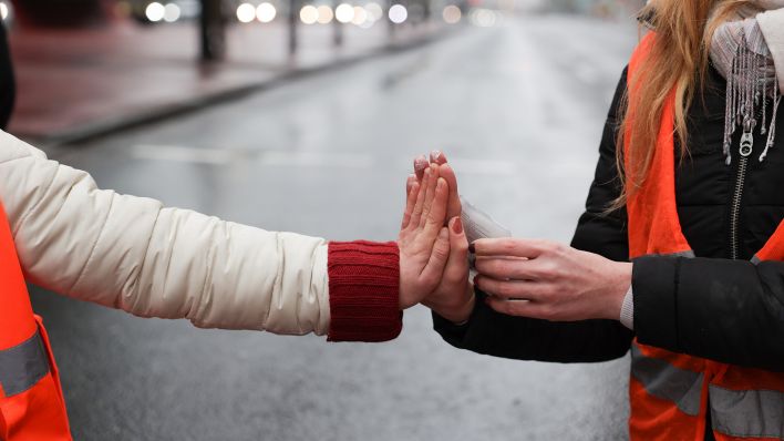 Klimaaktivisten sitzen am 05.12.2022 mit ihren Händen zusammengeklebt auf einer Straße am Potsdamer Platz und wärmen sich ihre Hände mit einem Wärmekissen. (Quelle: dpa/Jörg Carstensen)