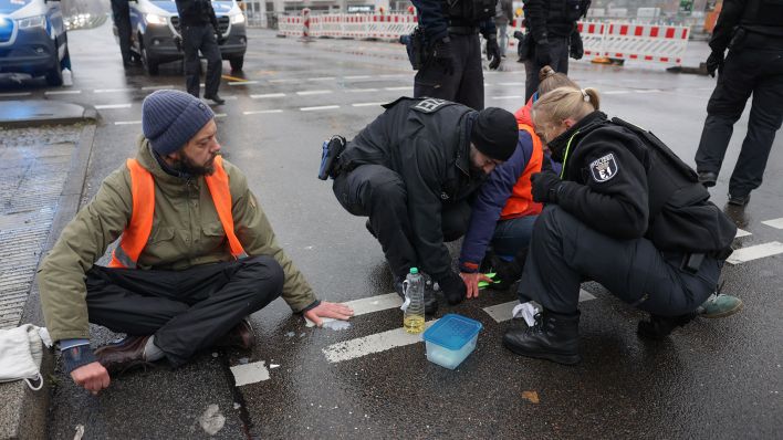 Polizisten lösen die Hand eines Klimaaktivisten vom Asphalt auf der Berliner Invalidenstraße