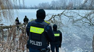 Polizisten fordern am 18.12.2022 Menschen dazu auf die zugefrorenen Karpfenteiche im Stadtteil Pankow zu verlassen. (Quelle: dpa/Jörg Carstensen)