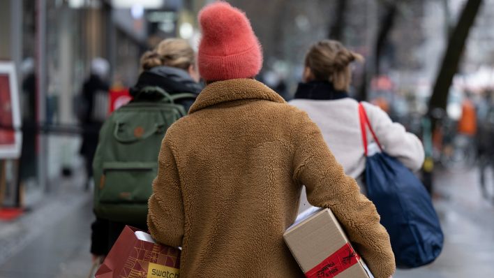 Eine Frau geht am 22.12.2022 über eine Einkaufsstraße in der Berliner City West und trägt eine Einkaufstasche und ein Paket in ihren Händen. (Quelle: dpa/Monika Skolimowska)