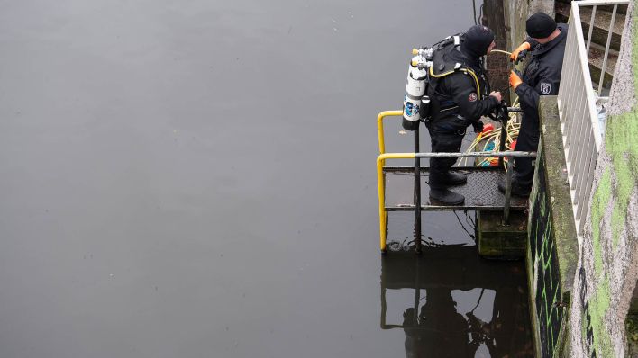 Ein Polizeitaucher bereitet sich mit Hilfe eines Kollegen an einem Kanal an der Treptower Straße auf einen Einsatz vor. (Quelle: dpa/Paul Zinken)