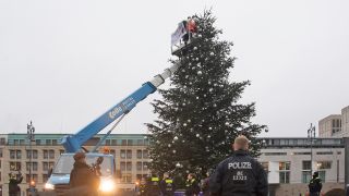 "Es ist nur die Spitze des Weihnachtsbaums" steht auf dem Transparent der Aktivisten der "Letzten Generation", die am 21.12.2022 die Spitze des Berliner Weihnachtsbaums entfernten. (Quelle: dpa/Paul Zinken)