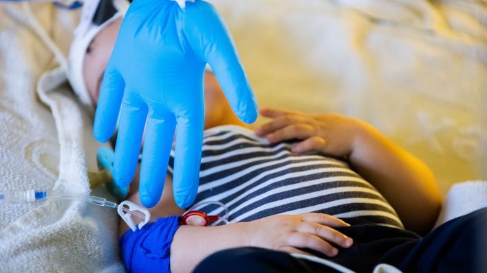 Ein aufgeblasener Handschuh hängt als Spielzeug vor dem Kind, das mit einem Atemwegsinfekt auf der Intensivstation liegt. (Quelle: dpa/Christoph Soeder)