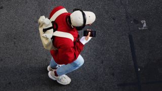 Ein junger Mann traegt Kopfhörer und blickt auf sein Smartphone, während er über eine Strasse geht (Quelle: Wolfram Steinberg/dpa)