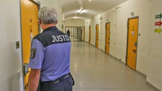 Justizbeamter im Flur der Untersuchungshaftanstalt Moabit in Berlin mit geschlossenen Zellentüren. (Quelle: imago images)