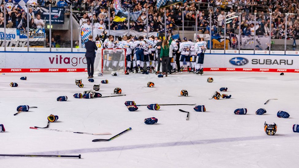 Zurückgelassene Eishockeyschläger und Handschuhe und die feiernde Mannschaft der Eisbären Berlin im Hintergrund (Imago Images/Eibner)