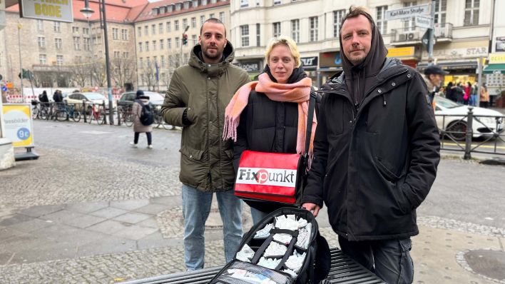 Das Neuköllner Team des Berliner Fixpunkts steht mit einem halb geöffneten Rucksack an einer Straße. Bild: rbb/Simon Wenzel