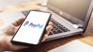 Symbolbild: Paypal Online Zahlungsservice und Banking Unternehmen auf einem Smartphone Display, das in der Hand vor einem Notebook auf einem Tisch gehalten wird. (Quelle: dpa/M. Bihlmayer)