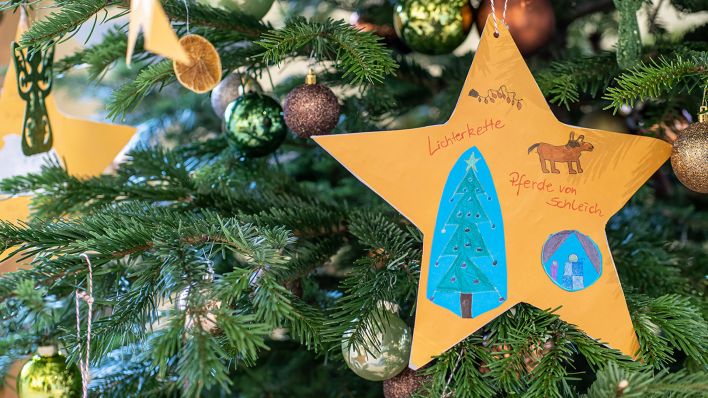 Ein Papierstern, beschriftet mit dem Weihnachtswunsch nach einer Lichterkette, hängt an einem Tannenbaum (Quelle: rbb/Thomas Ernst)