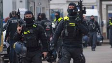 Einsatzkräfte der Polizei gehen mit ihren Waffen in der Hand über ein Gelände in Lichtenberg. Mit einer Razzia gehen die Beamten gegen mutmaßliche, international operierende Drogenhändler vor. (Quelle: Paul Zinken/dpa)