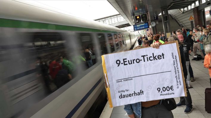 Archiv: Ein Demonstrant steht mit einem überdimensionalen 9-Euro-Ticket bei der Zug-Demo «Sonderzug zu Lindner» am Bahnhof Gesundbrunnen vor einem einfahrenden Zug. (Foto: Jörg Carstensen/dpa)