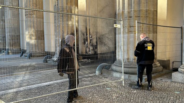 Zwei Personen stellen am 16.01.2023 Bauzäune an einer Säule des Brandenburger Tores auf. (Quelle: dpa/Paul Zinken)