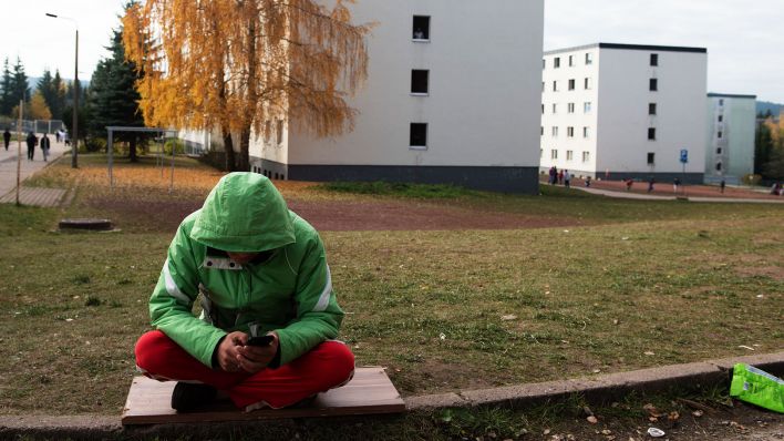 Symbolbild:Ein junger Geflüchteter sitz vor den Gebäuden einer Erstaufnahmestelle.(Quelle:dpa/S.Kahnert)
