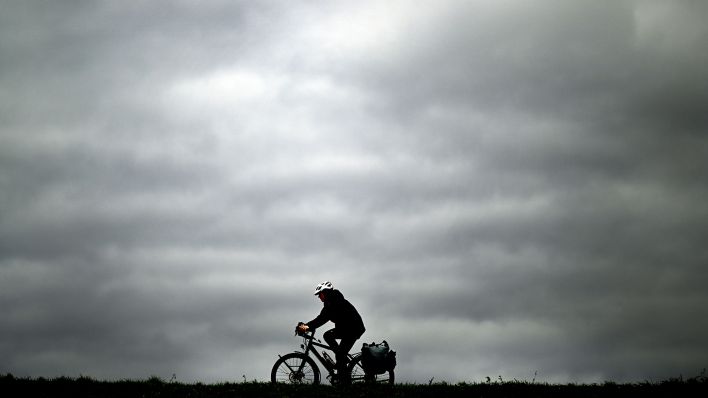Ein Radfahrer fährt vor dem Grauen Wolkenhimmel, Archivbild (Quelle: DPA/Federico Gamberini)