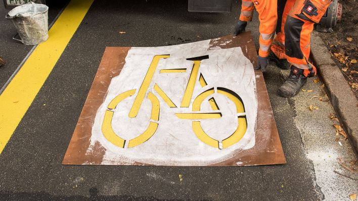 Ein Mitarbeiter einer Straßenunterhaltungsfirma hält eine Schablone über ein Fahrradsymbol. (Quelle: dpa/Daniel Bockwoldt)