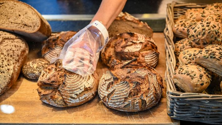 Eine Verkäuferin greift mit Handschuhen nach einem Brot. (Quelle: dpa/Jens Kalaene)