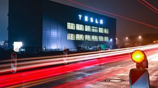 Fahrzeuge fahren am frühen Morgen auf einer Straße vor dem Gebäude der Batteriefertigung des US-Elektroautobauers Tesla vorbei. (Quelle: dpa/Patrick Pleul)