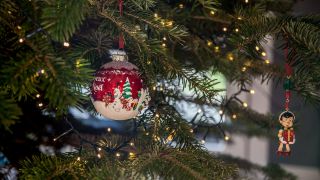 An einem Weihnachtsbaum ist der Christbaumschmuck aufgehängt man sieht die Weihnachtskugel hängen und die Lichterketten leuchten. (Quelle: dpa/K. Schmitt)