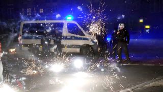 Polizeibeamte stehen hinter explodierendem Feuerwerk. (Quelle: dpa/Julius-Christian Schreiner)
