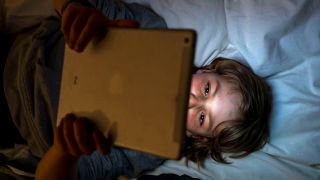 Symbolbild:Ein Junge schaut sich etwas auf einem Tablet im Dunklen an.(Quelle:imago images/J.Tack)