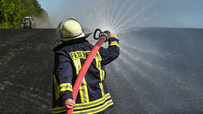 Symbolbild: Ein Feuerwehrmann löscht letzte Glutnester auf einem abgebrannten Stoppelfeld. (Quelle: dpa/Patrick Pleul)