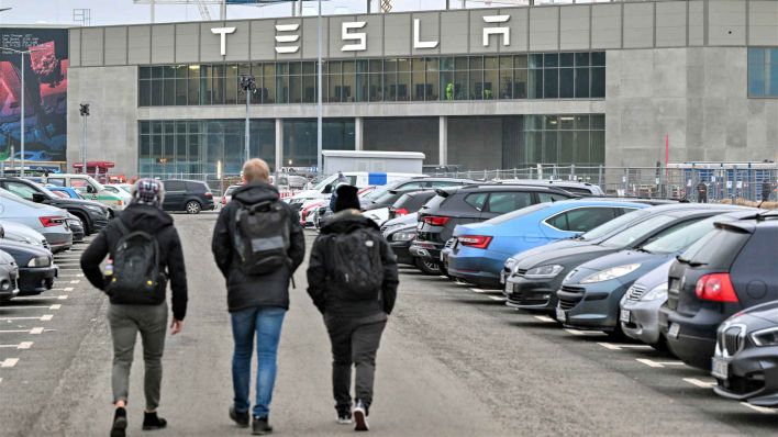 Archiv: Mitarbeiter gehen über einen Parkplatz in Richtung der Tesla Gigafactory Berlin-Brandenburg vom US-Elektroautobauer Tesla. (Foto: dpa)