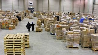 Freiwillige gehen am 09.02.2023 zwischen lokal gespendeten Hilfsgütern für die Erdbebenopfer in der Türkei in einem Lager nahe dem Berliner Flughafen BER Berlin-Brandenburg. (Quelle: dpa/Carsten Koall)