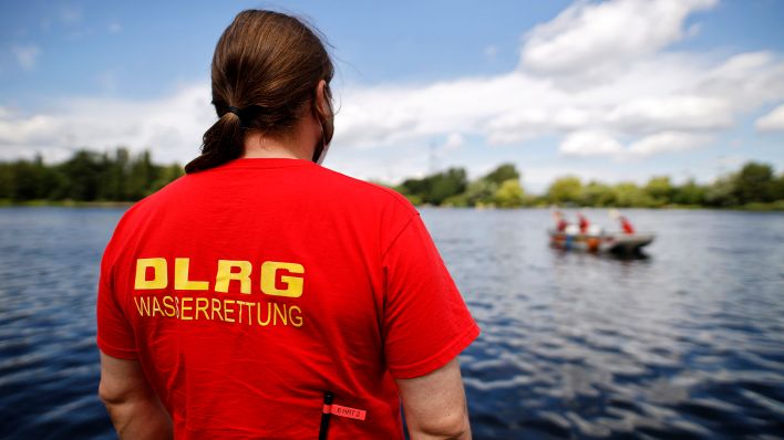 Symbolbild:Eine ehrenamtliche Kraft des DLRG vor einem See mit Rettungsboot.(Quelle:dpa/Geisler-Fotopress)